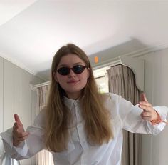 a woman wearing sunglasses is standing in front of a mirror and giving the thumbs up sign