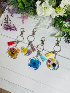 four keychains with different designs on them sitting next to flowers and greenery