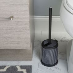 a toilet brush holder in the corner of a bathroom next to a white toilet and gray rug