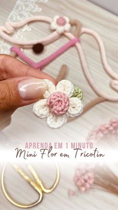 a hand holding a flower on top of a table next to some crochet