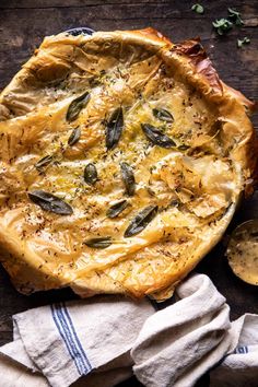 a quiche with cheese, herbs and sauces on a wooden table next to napkins