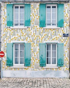 an old building with blue shutters and green shutters on the windows is decorated with yellow flowers