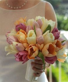 a woman holding a bouquet of flowers in her hand and wearing a white dress with pink, yellow and orange tulips