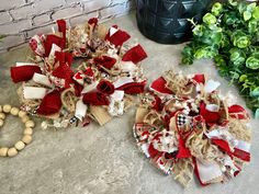 two red and white wreaths sitting next to each other on the ground near some potted plants