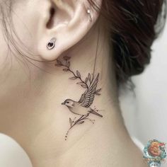 a woman's neck with a small bird and flower tattoo on the back of her neck