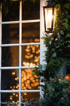 a lantern is lit on the outside of a house with christmas lights in the window