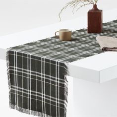 a plaid table runner with a coffee cup and vase on the end, next to it