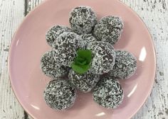 a pink plate topped with chocolate donuts covered in powdered sugar and green leaf