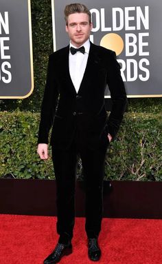 a man in a tuxedo and bow tie standing on a red carpet with his hands in his pockets