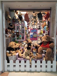 teddy bears are displayed in the window of a toy store with white picket fence around them