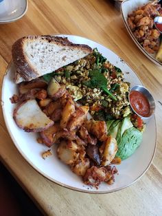 a white plate topped with lots of food on top of a wooden table next to other plates