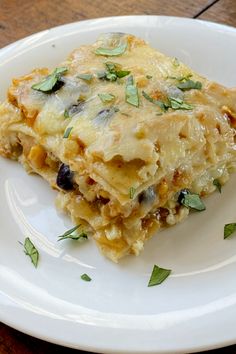 a white plate topped with lasagna covered in cheese and herbs on top of a wooden table