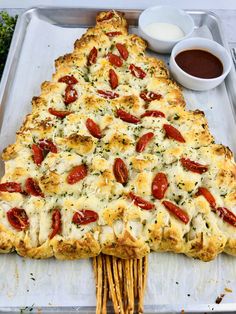 a cheesy pizza with tomatoes and cheese on a tray next to dipping sauce