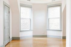 an empty room with two windows and hard wood floors