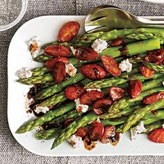 asparagus with tomatoes and goat cheese on a white plate next to silverware