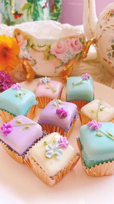 some cupcakes are sitting on a plate with teapot and flowers in the background