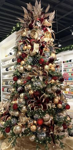 a christmas tree with gold and red ornaments on it's top, in a store