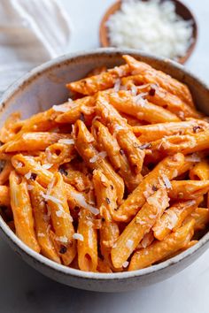 a bowl filled with pasta covered in sauce and parmesan cheese on the side