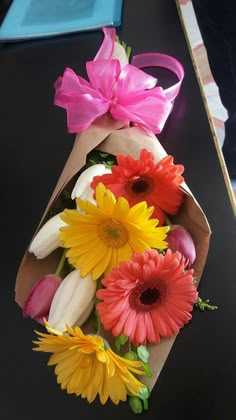 a bouquet of flowers is wrapped in brown paper with pink and yellow ribbons on it