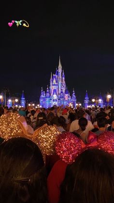 a crowd of people standing in front of a castle at night with the lights on