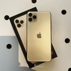 two gold iphones sitting next to each other on top of a white table with black dots