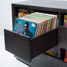 a record player's storage unit with vinyl records in the drawer and an album on top