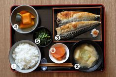 a tray with rice, carrots, fish and other foods in it on top of a wooden table