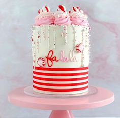 a white and red striped cake with candy canes on top, sitting on a pink pedestal