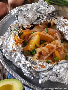 an aluminum foil covered plate with food on it and vegetables in the background, along with two forks