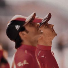 two men in red shirts and hats are looking at something off to the side with one man's head tilted