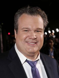 a close up of a person wearing a suit and tie smiling at the camera with people in the background