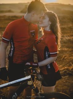 a man and woman standing next to each other in front of a bike with the sun behind them