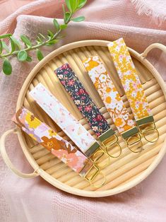 five colorful paper clips sitting on top of a bamboo tray next to a plant and pink cloth