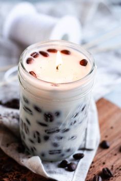 a candle that is sitting in a jar on a table next to some coffee beans