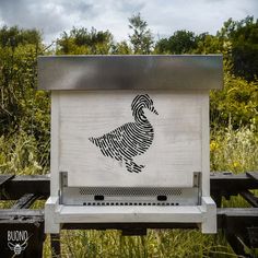 a sign with a rooster drawn on it in front of some tall grass and trees