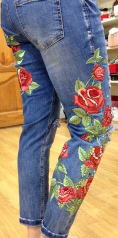 a woman's jeans with red roses and green leaves on them, showing the bottom part of her legs