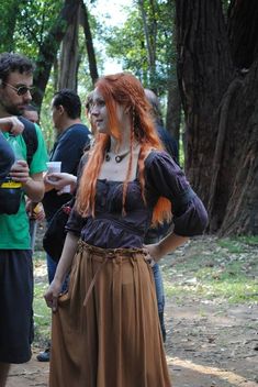 a woman with long red hair standing next to a group of people in the woods