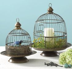 two birdcages with candles and flowers in them sitting on a table next to each other