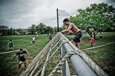 a man climbing up the side of a roped off fence while other people watch