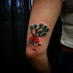 a woman's arm with a small tree and red ball tattoo on the left inner arm