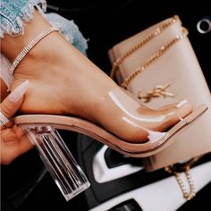 a woman's feet wearing clear heels and holding a purse