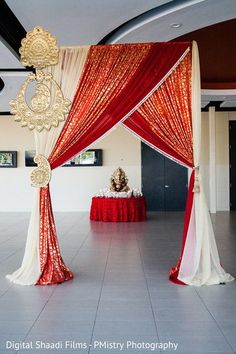 a red and white wedding setup with draping on the ceiling, decorated with gold accents