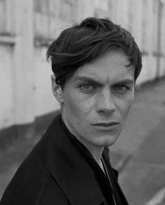 a black and white photo of a man in a suit standing on the side walk