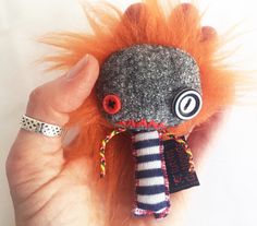 a hand holding a small stuffed animal with orange hair and eyeballs on it's face