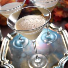 two martini glasses filled with white wine on top of a silver platter next to autumn leaves