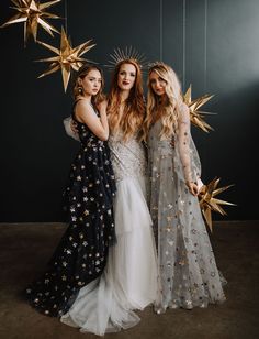 three beautiful women standing next to each other wearing dresses with stars hanging from the ceiling