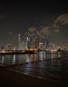 the city skyline is lit up at night with lights reflecting off the water in front of it