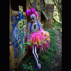 a creepy clown sitting on the side of an old train car in a colorful dress