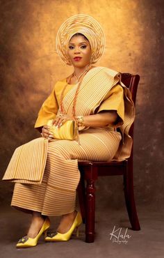 a woman sitting on top of a wooden chair wearing a yellow dress and headdress