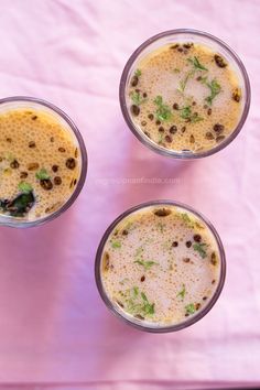 three glasses filled with liquid and topped with green garnish on a pink cloth